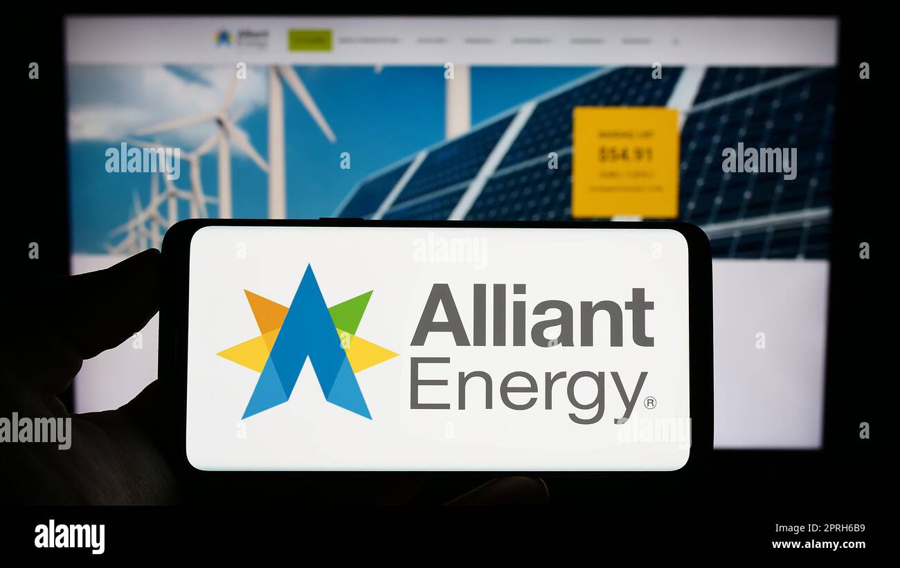 Personne tenant un téléphone portable avec le logo de la société américaine alliant Energy Corporation à l'écran en face de la page Web d'affaires. Mise au point sur l'affichage du téléphone. Banque D'Images