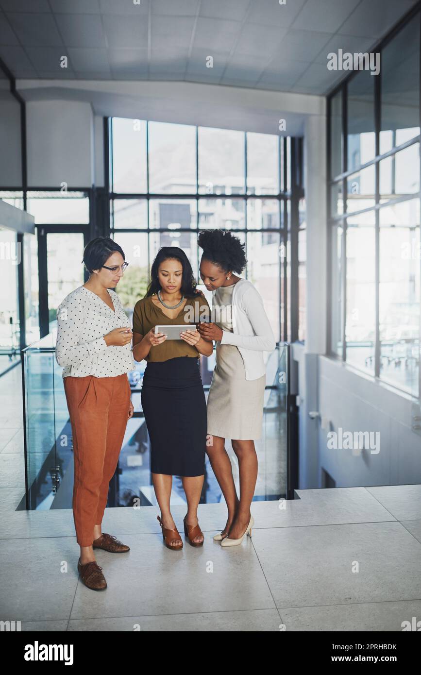 Beaucoup de mains font le travail léger. Prise de vue en longueur de trois femmes d'affaires regardant une tablette au bureau. Banque D'Images