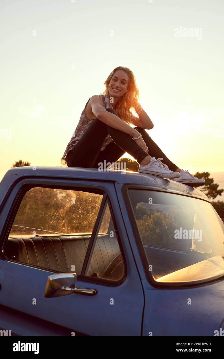 Free...its la seule façon d'être. Portrait d'une jeune femme attrayante assise sur le capot de son camion lors d'un voyage en voiture. Banque D'Images