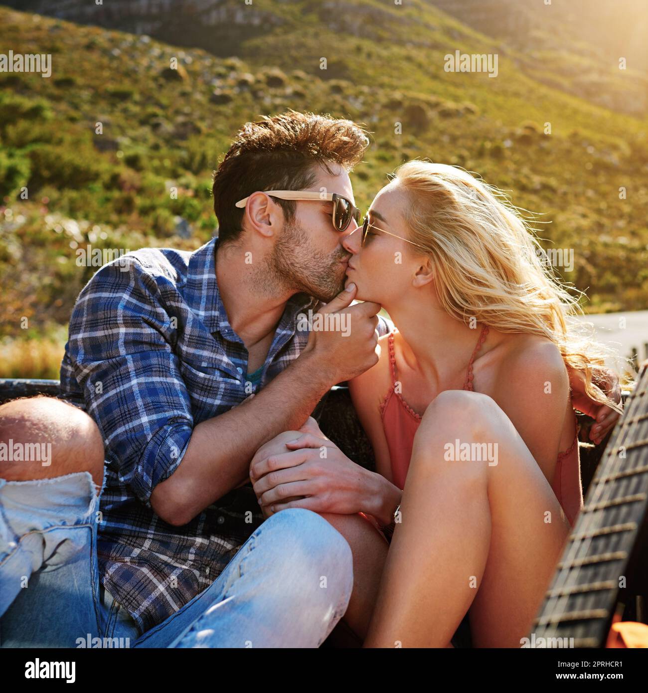 Un jeune couple qui partage un baiser tout au dos d'un pick-up fait l'expérience d'un tout nouveau côté de l'amour sur la route. Banque D'Images