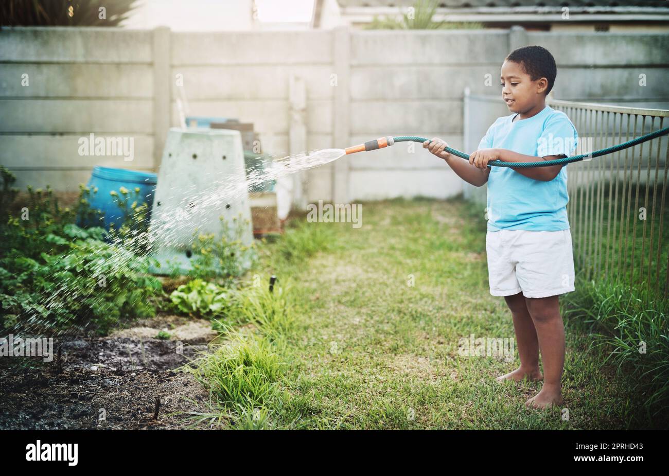 L'enfer grandit avec une passion pour les plantes. Un petit garçon utilisant un tuyau d'arrosage pour arroser le jardin à l'extérieur. Banque D'Images