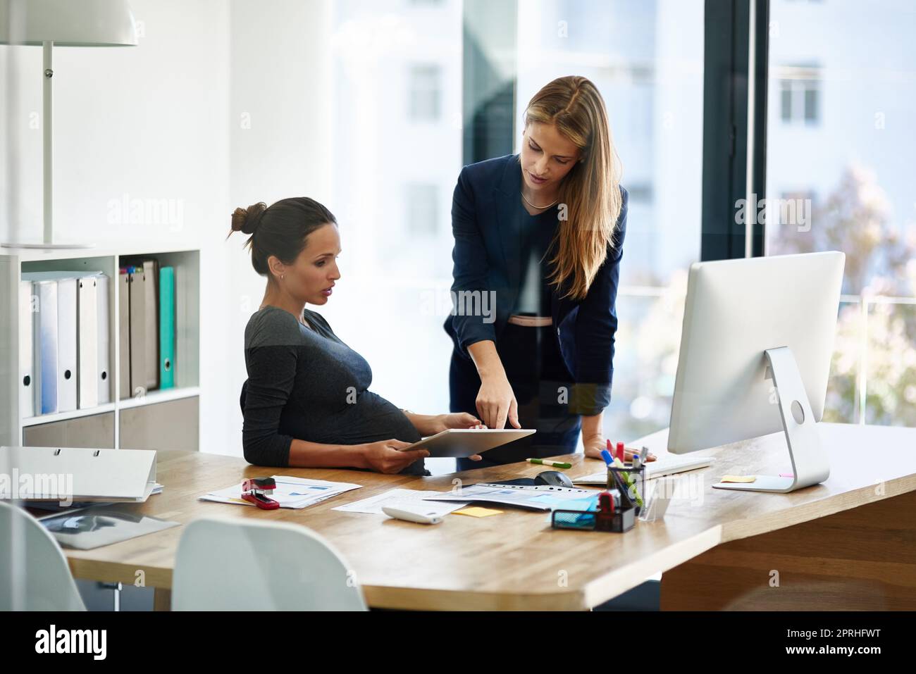 Trouver un équilibre entre le travail et l'attente. Une femme d'affaires enceinte et un collègue utilisent une tablette numérique ensemble dans un bureau. Banque D'Images