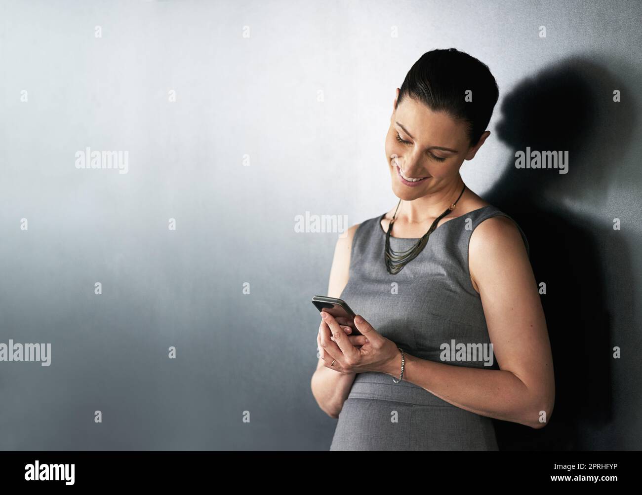 Envoi d'une mise à jour de projet. Photo en studio d'une femme d'affaires utilisant son téléphone portable sur fond gris. Banque D'Images