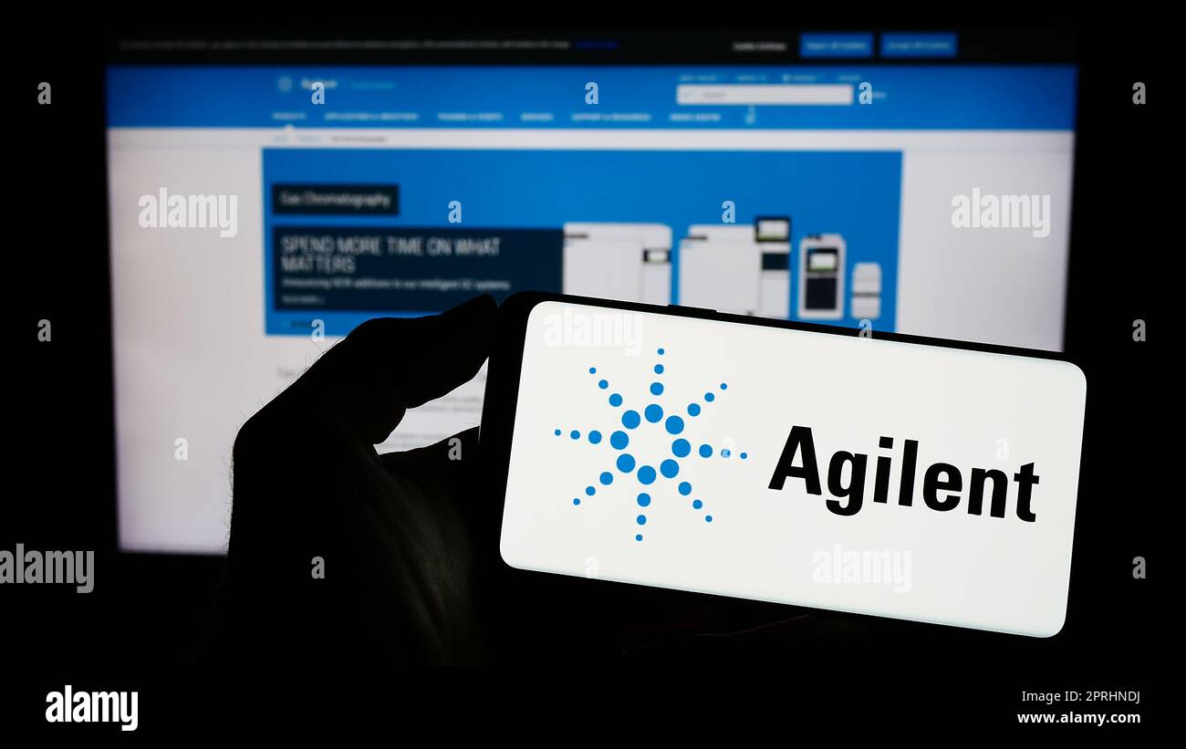 Personne possédant un smartphone portant le logo de la société américaine Agilent technologies Inc. À l'écran, devant le site Web. Mise au point sur l'affichage du téléphone. Banque D'Images