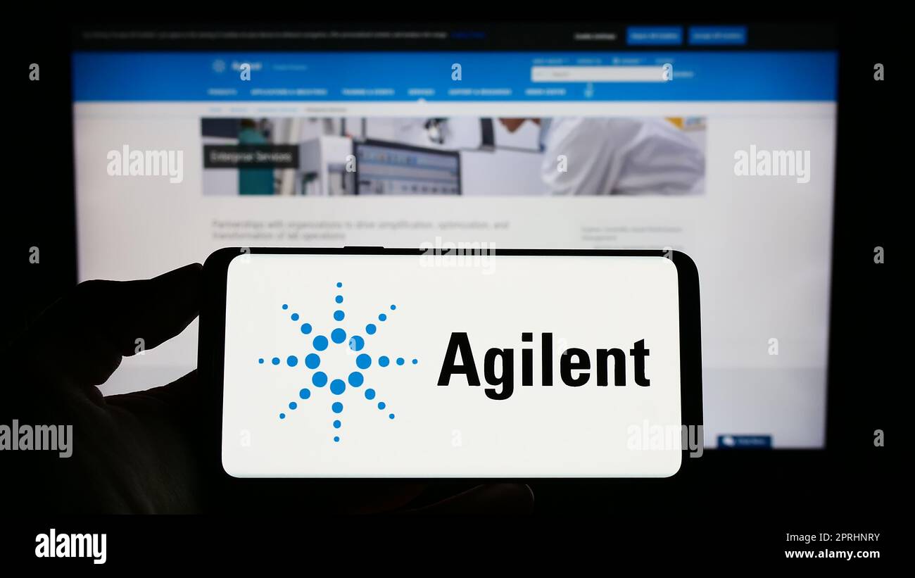 Personne tenant un téléphone portable avec le logo de la société américaine Agilent technologies Inc. À l'écran en face de la page Web d'affaires. Mise au point sur l'affichage du téléphone. Banque D'Images