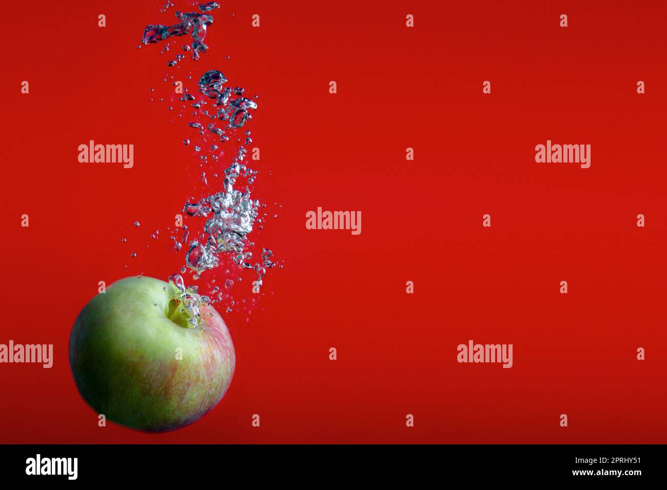 pomme sur fond rouge éclaboussant dans l'eau les bulles fraîches éclabousser les fruits Banque D'Images