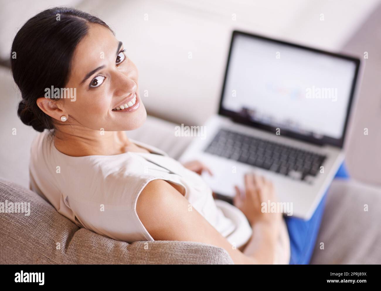 En ligne où et quand. Prise de vue sur l'épaule d'une jeune femme assise sur un canapé à l'aide d'un ordinateur portable Banque D'Images