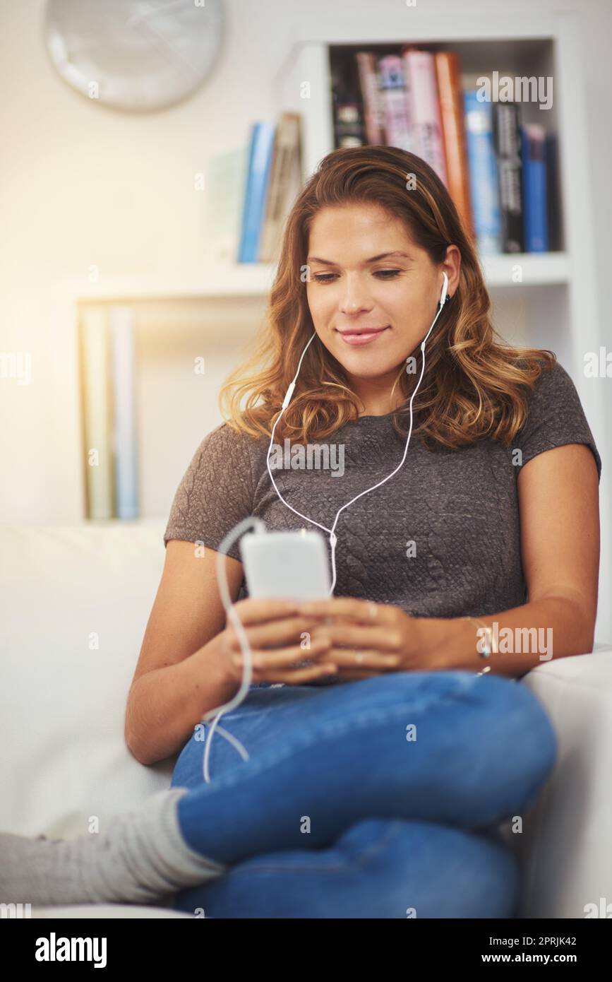 Téléchargement de sa liste de lecture du week-end. Une jeune femme écoute de la musique sur son téléphone à la maison. Banque D'Images