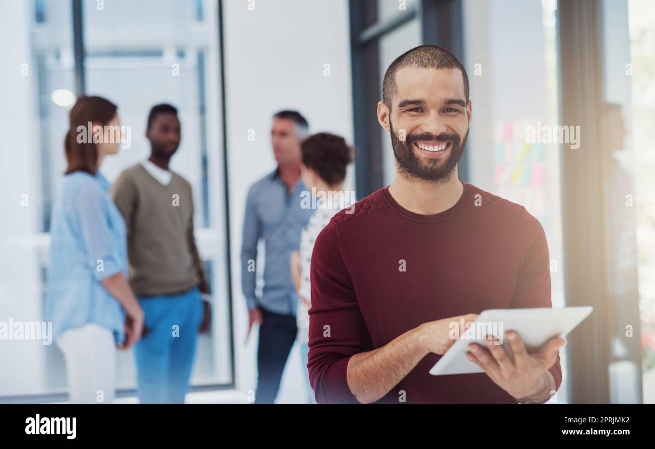 Je peux tout faire en déplacement. Portrait court d'un jeune homme d'affaires travaillant au bureau avec ses collègues en arrière-plan. Banque D'Images