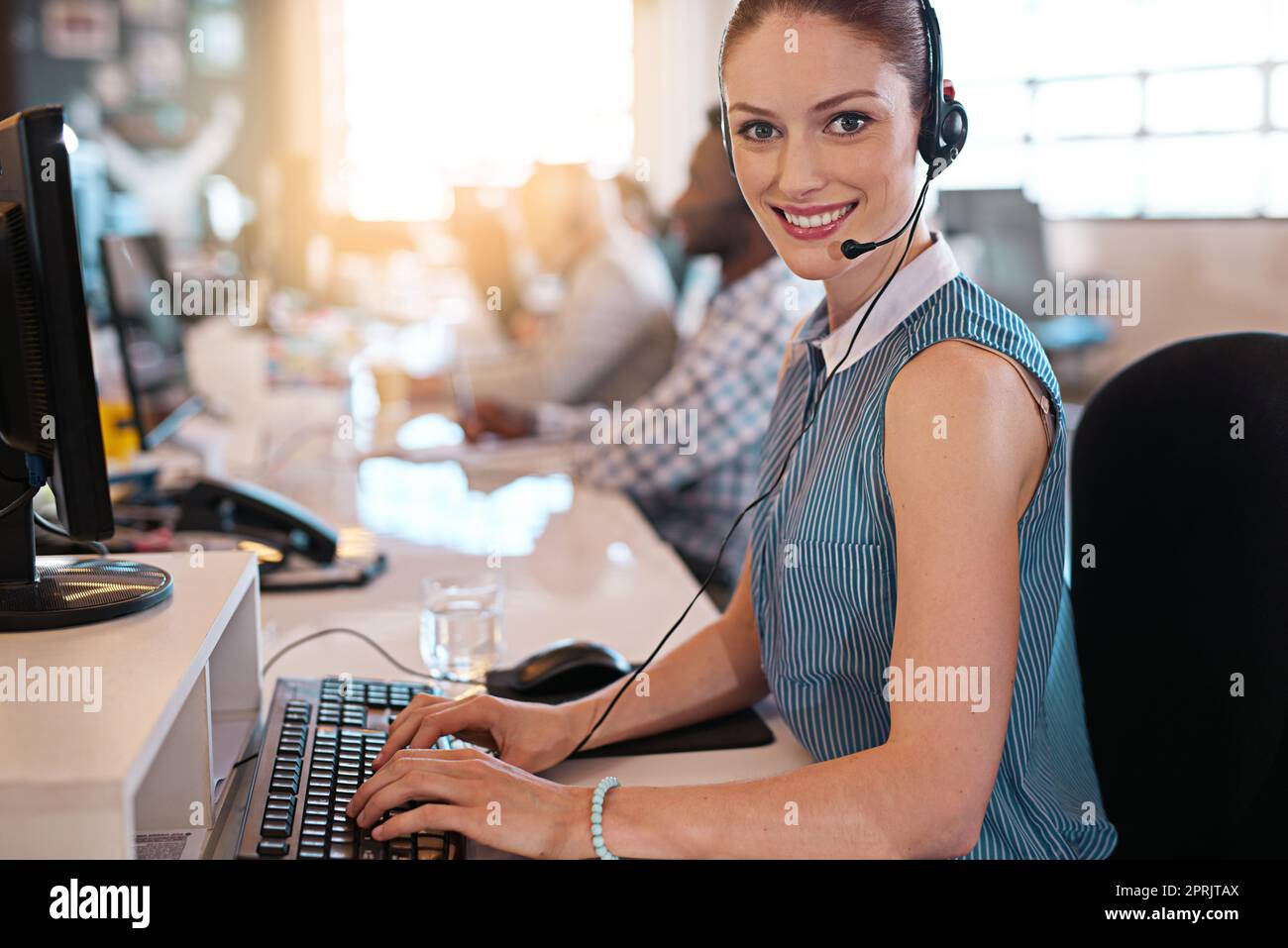 En attente de votre appel. Portrait d'un agent de centre d'appels heureux travaillant sur son ordinateur au bureau. Banque D'Images