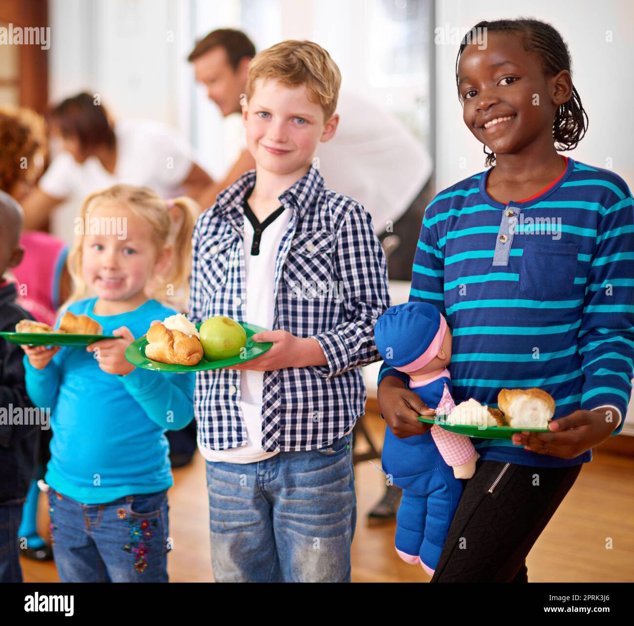 S'assurer qu'ils mangent sainement. Portrait des enfants avec des assiettes de nourriture avec des bénévoles servant de la nourriture en arrière-plan. Banque D'Images