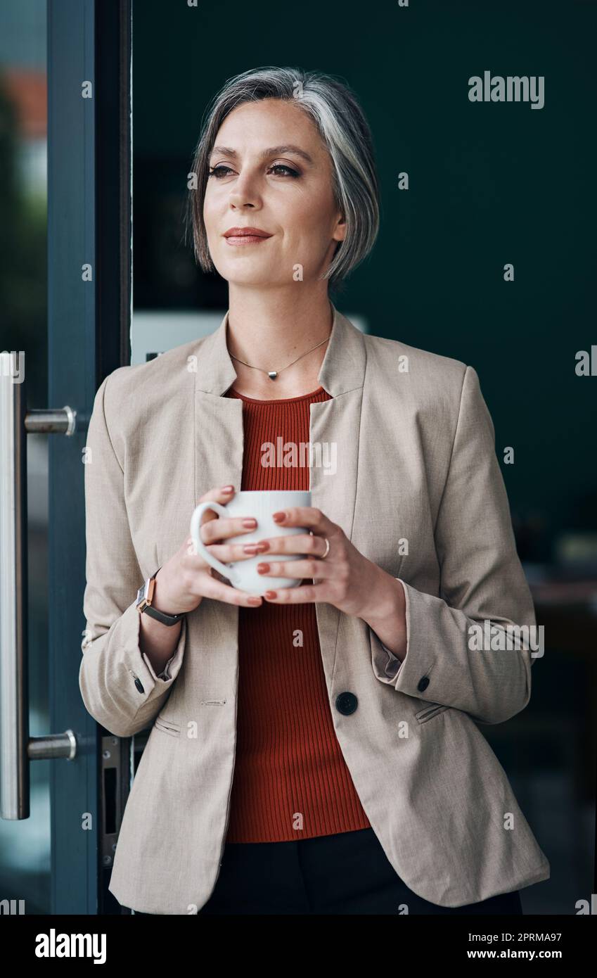 Les bonnes idées commencent par le café. une femme d'affaires attirante et mûre debout seule et appréciant une tasse de café dans son bureau à la maison Banque D'Images