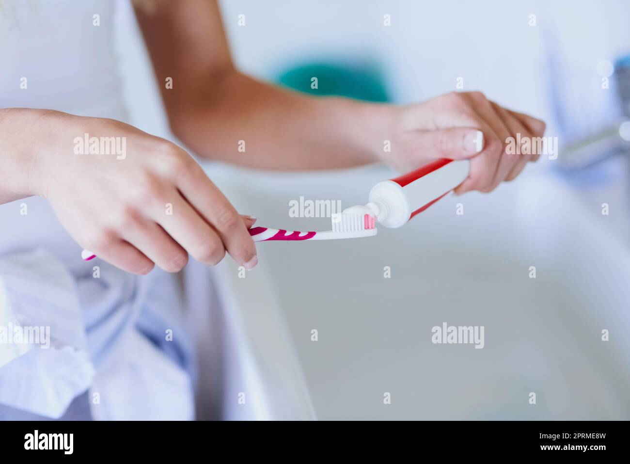 Des dents saines sont une habitude quotidienne. Une femme qui ne peut pas être identifiée met du dentifrice sur sa brosse à dents à la maison. Banque D'Images