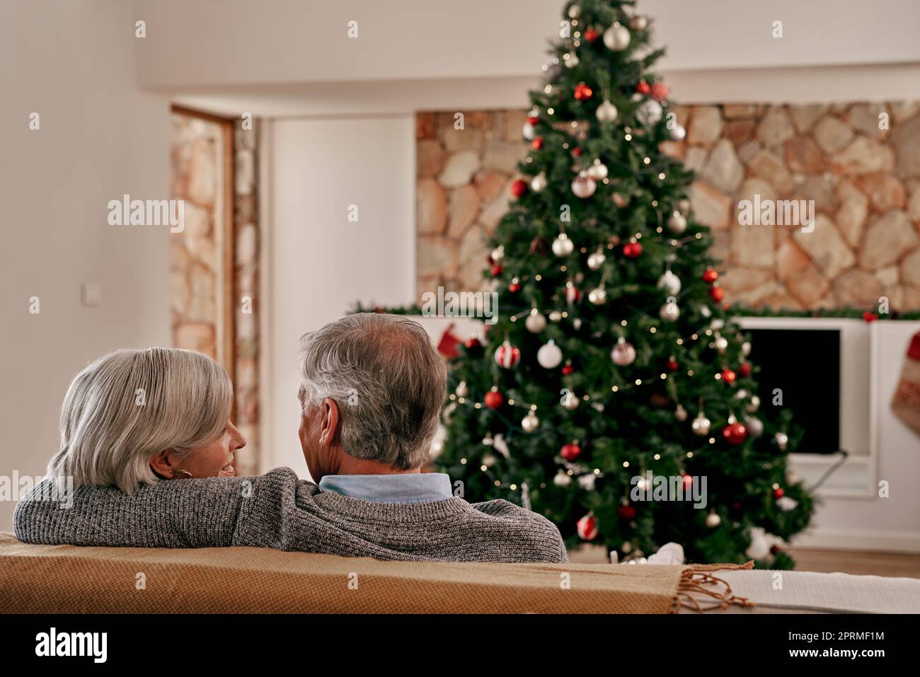 Maintenant étaient officiellement prêts pour Noël. Vue arrière d'un couple adulte méconnu assis ensemble sur un canapé se tenant l'un contre l'autre tout en regardant un Banque D'Images