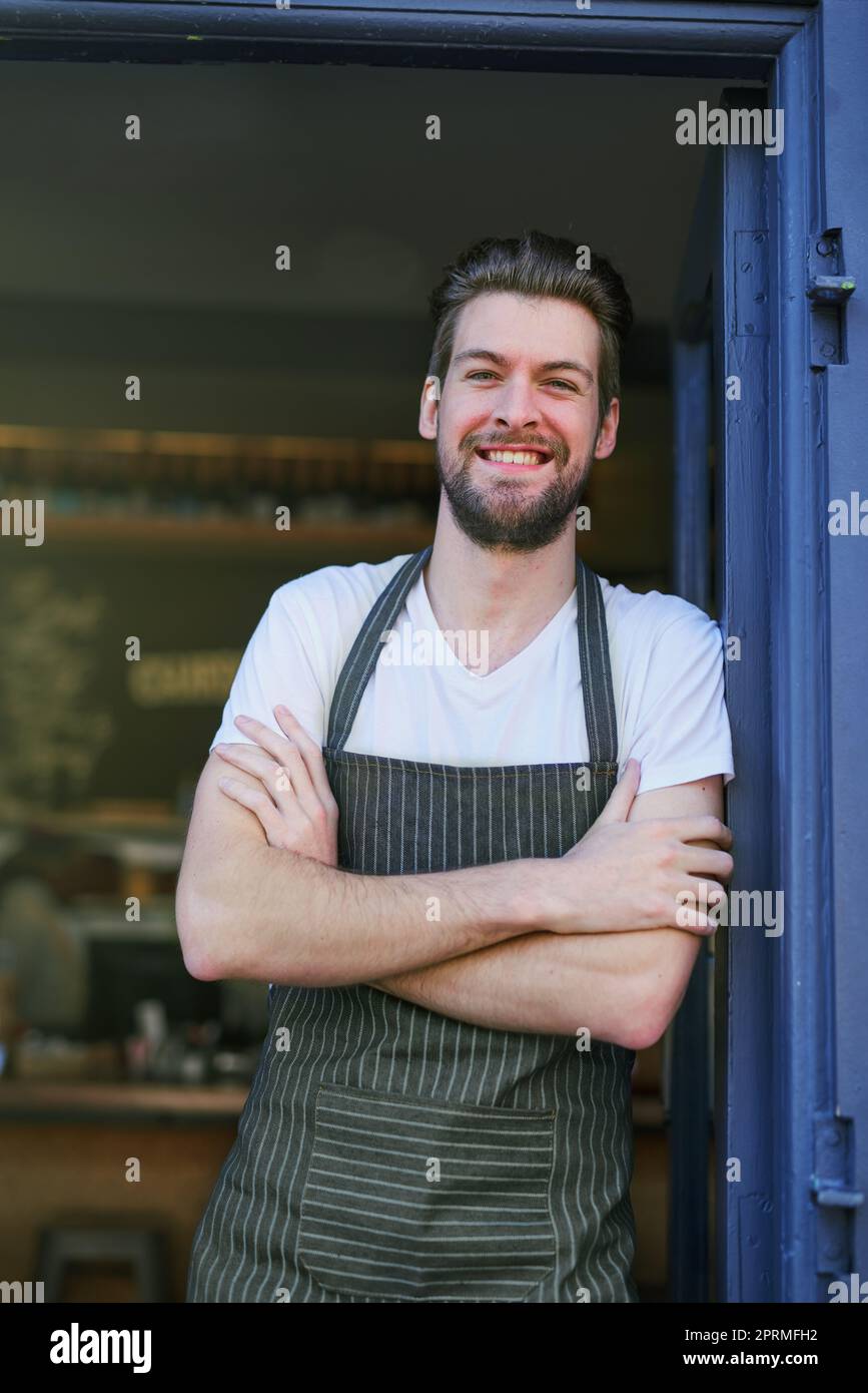 Entrez, prenez votre café. Portrait d'un jeune homme debout à l'entrée de son café. Banque D'Images