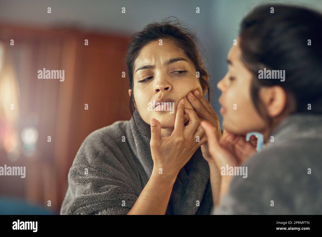 C'est un endroit que je vois. Une jeune femme frognant tout en examinant une imperfection sur sa peau dans le miroir. Banque D'Images