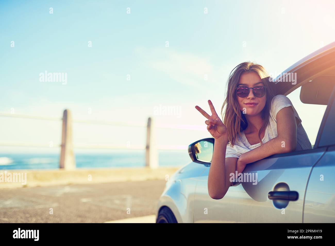 Le voyage sur route est une question de liberté. Portrait d'une jeune femme qui vous donne le signe de la paix tout en étant assise dans sa voiture. Banque D'Images