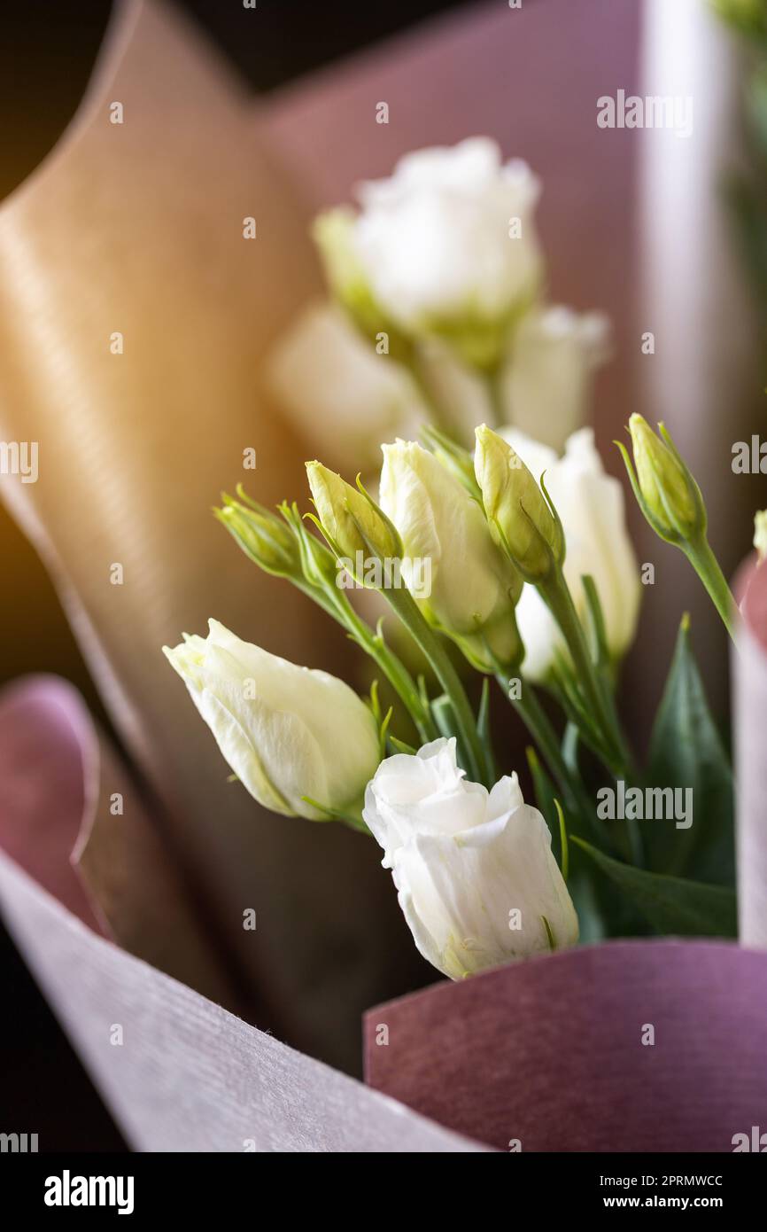 Gros plan de fleurs d'eustoma blanc dans un bouquet enveloppé de papier rose. Banque D'Images
