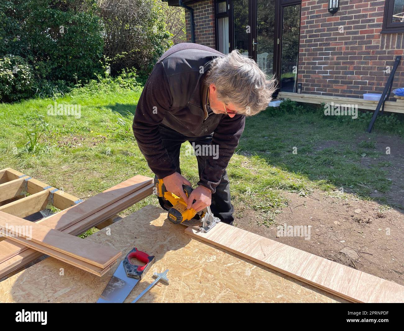 Un charpentier utilise un outil électrique sans fil pour couper une longueur de bois.Outdoor dans un jardin Banque D'Images