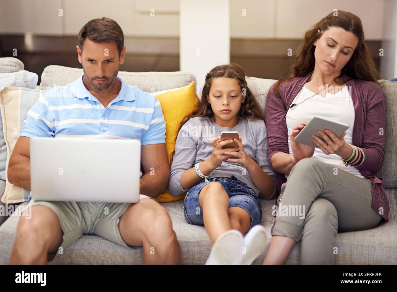 Laissez leurs appareils profiter du meilleur d'eux. Une famille assise sur le canapé à la maison. Banque D'Images