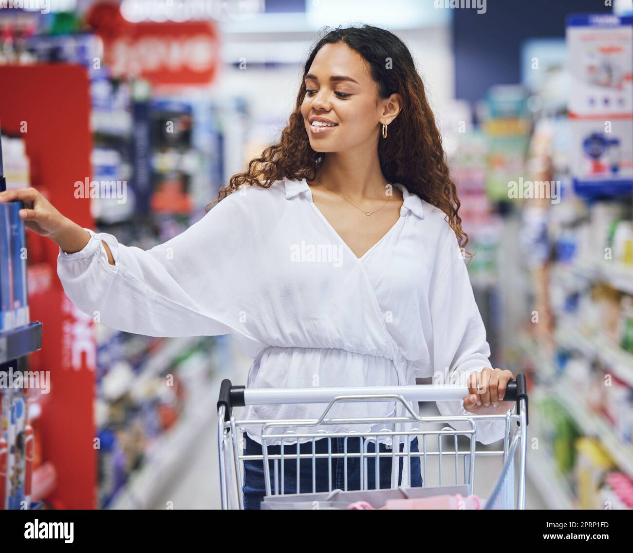 Le client, l'acheteur et le consommateur magasinent pour acheter des produits d'épicerie dans un supermarché, un centre commercial ou un point de vente au détail. Bonne femme qui pousse le chariot dans l'allée pour acheter des produits de vente, des articles à prix réduit et des offres de marque Banque D'Images