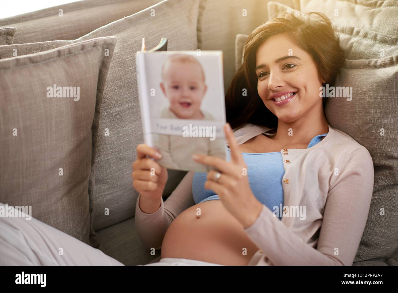 Lire un livre de bébé meilleur vendeur. Une jeune femme enceinte lisant un livre de bébé à la maison. Banque D'Images