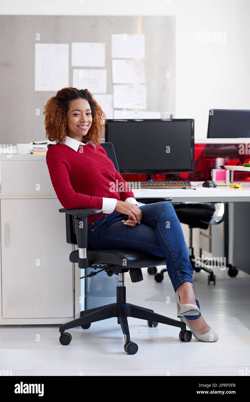 Shes heureux dans sa carrière. Portrait d'une jeune femme assise à son poste de travail dans un bureau Banque D'Images