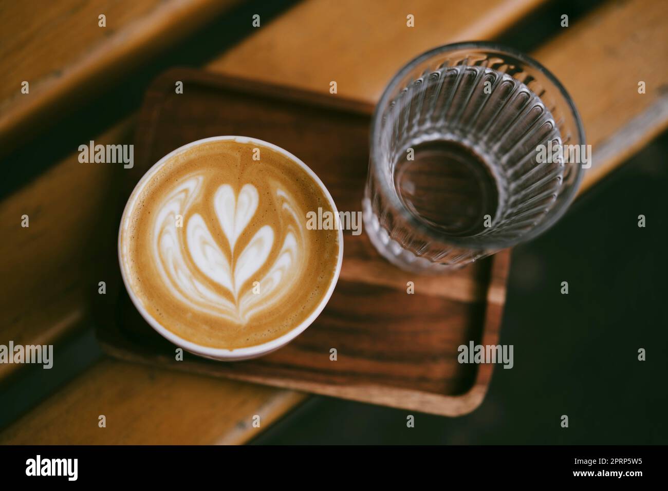 Cappuccino chaud dans une tasse sur un plateau en bois à côté d'un verre d'eau claire Banque D'Images