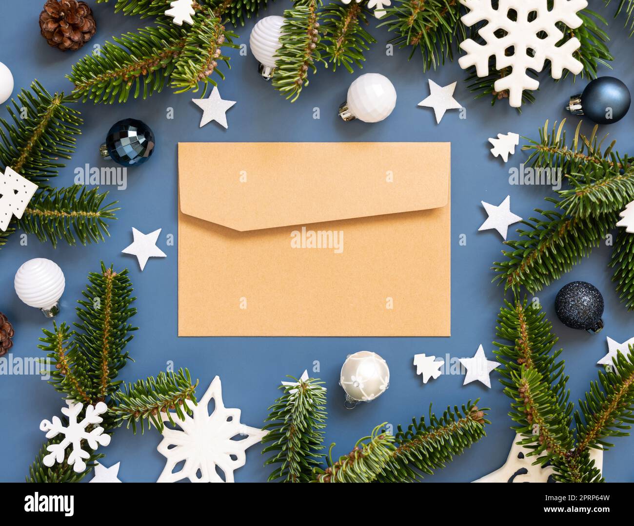 Enveloppe de papier artisanal sur fond bleu près des décorations de Noël blanches et des branches de sapin Banque D'Images