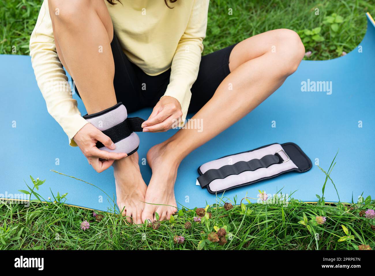 Une fille sportive fait un étirement dans la nature dans l'air frais, la fille pend des poids sur elle-même pour une meilleure étude des exercices. Une femme fait du yoga dans le parc, assise sur l'herbe sur un tapis de yoga. Banque D'Images