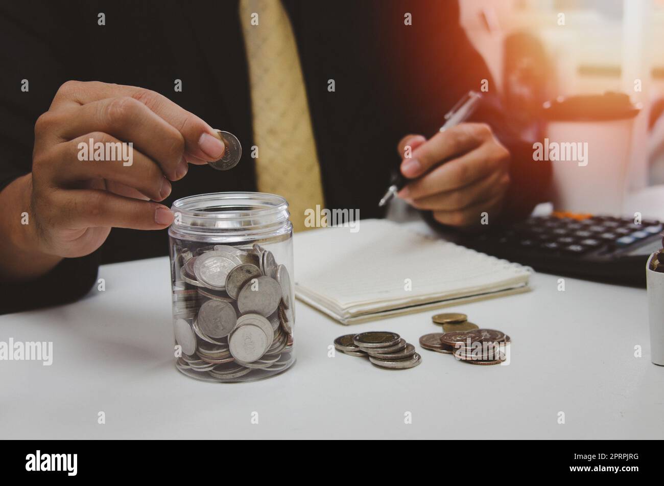 Homme à la main de mettre de l'argent pièce et de prendre note des revenus et des dépenses et de travailler pour économiser de l'argent pour la croissance future des affaires, de l'éducation et de la retraite. Banque D'Images