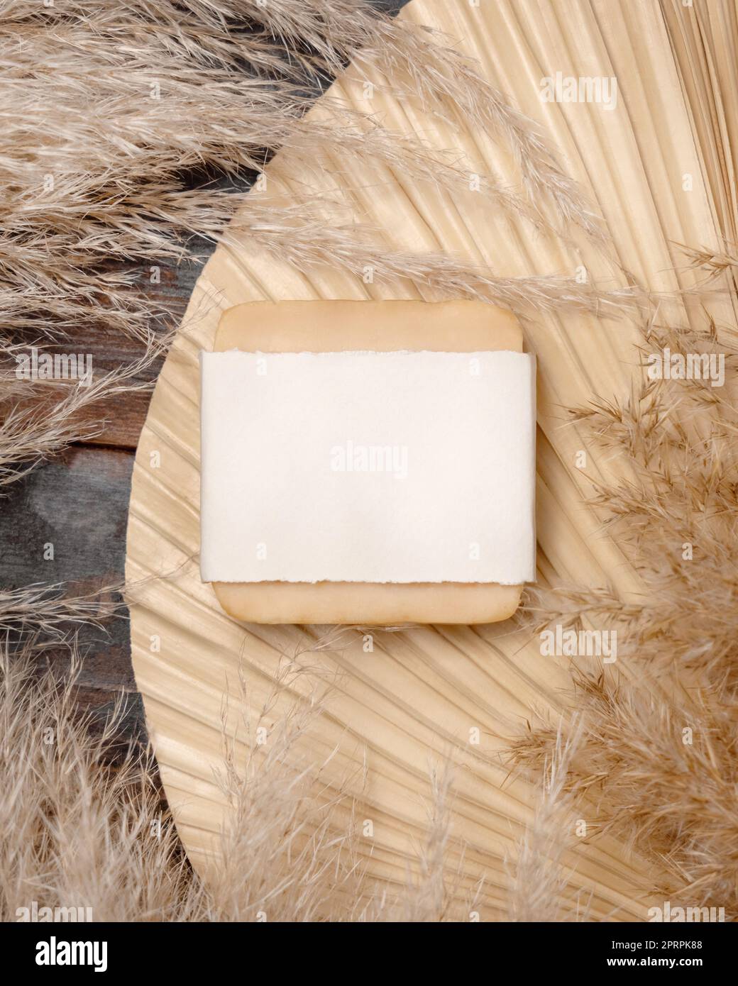 Porte-savon avec étiquette vierge sur la feuille de palmier séchée près de l'herbe de pampas vue de dessus. Maquette d'étiquette Banque D'Images