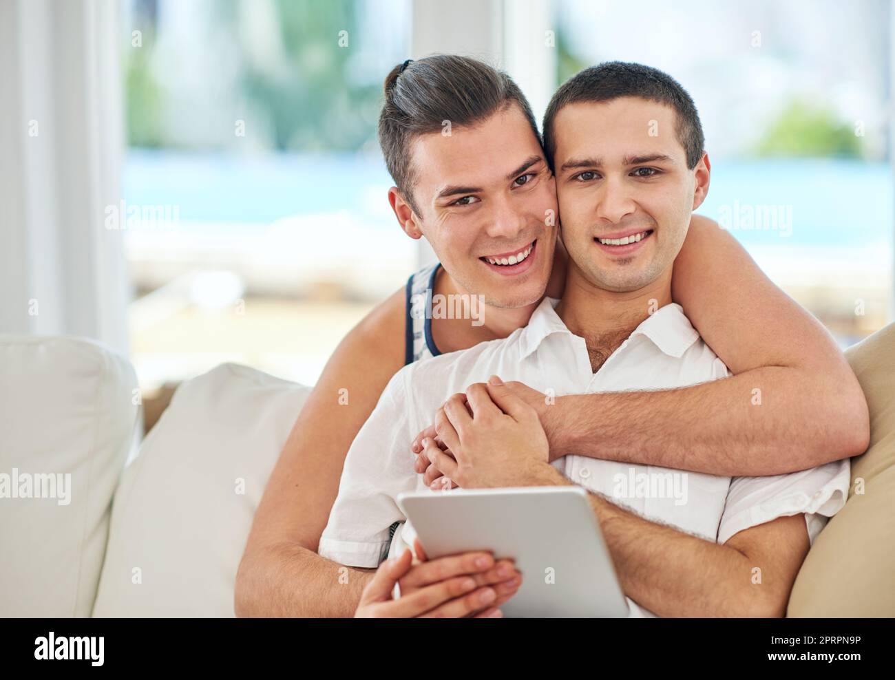 Tous les sourires et l'amour. Portrait d'un couple gay affectueux utilisant une tablette numérique tout en se relaxant sur le canapé à la maison Banque D'Images