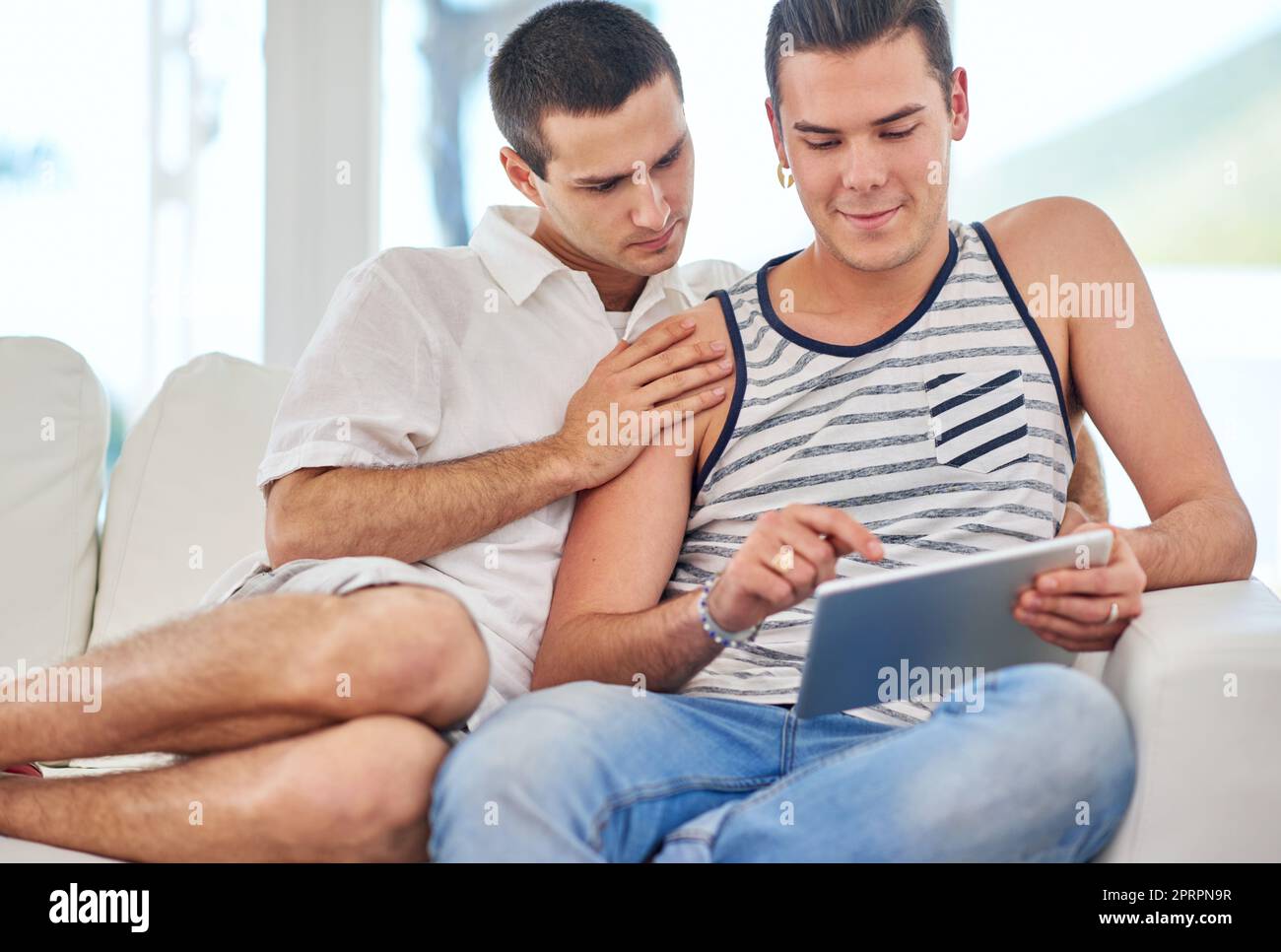 Prendre le plaisir dans les petits moments. Un couple gay utilisant une tablette numérique tout en se relaxant sur le canapé à la maison Banque D'Images