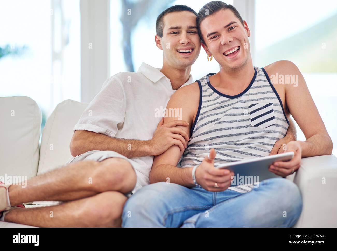 Nous nous faisons rire les uns les autres. Portrait d'un couple gay utilisant une tablette numérique tout en se relaxant sur le canapé à la maison. Banque D'Images