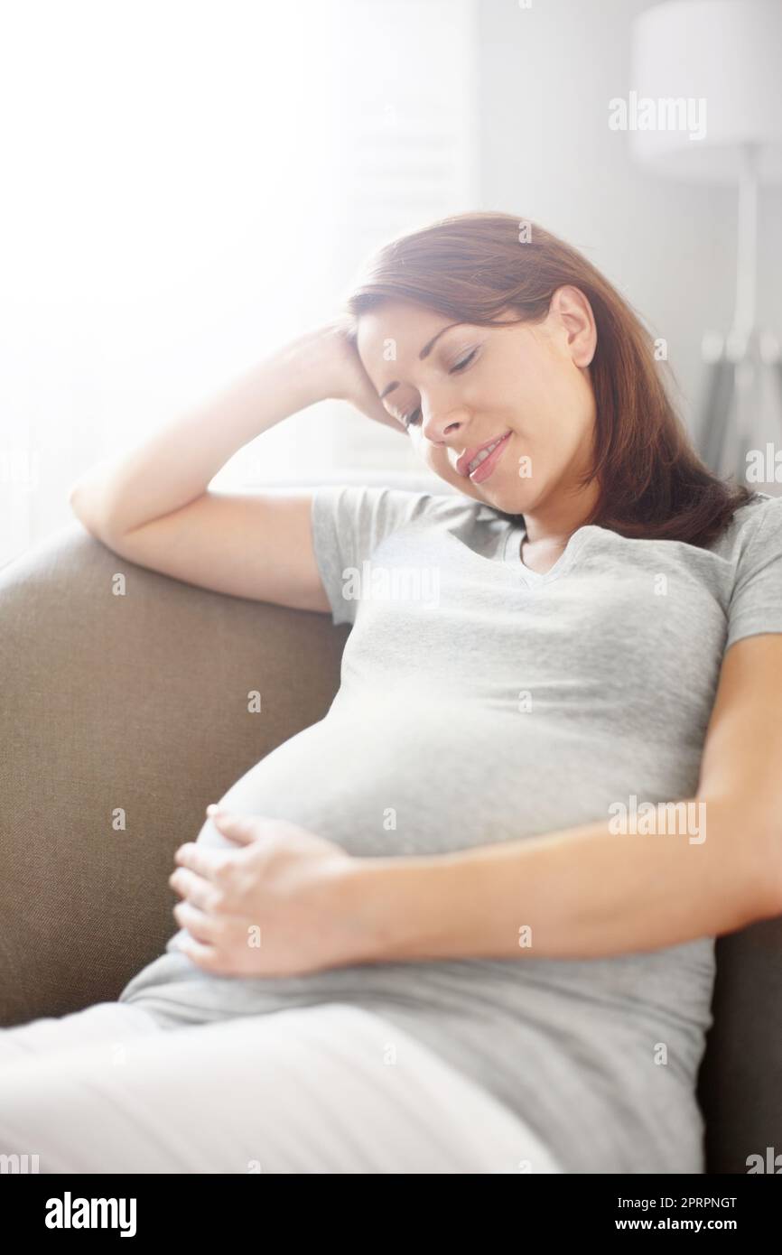 Shes va être une grande mère. Jeune femme enceinte assise dans son salon tout en tenant son ventre. Banque D'Images