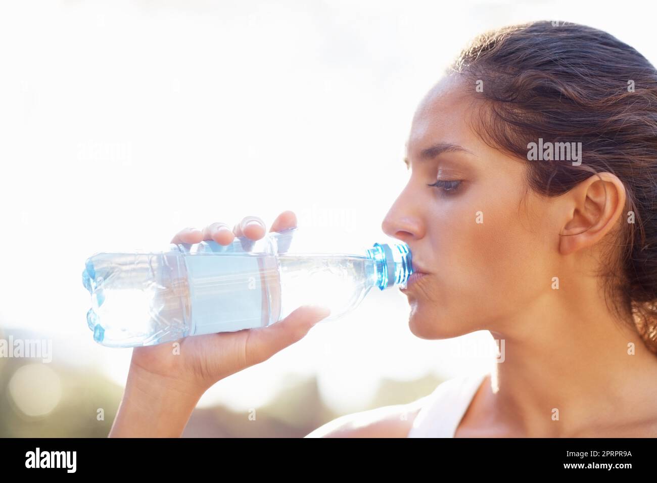 Une jeune femme boit de l'eau en bouteille. Gros plan de la jeune femme qui boit de l'eau en bouteille. Banque D'Images