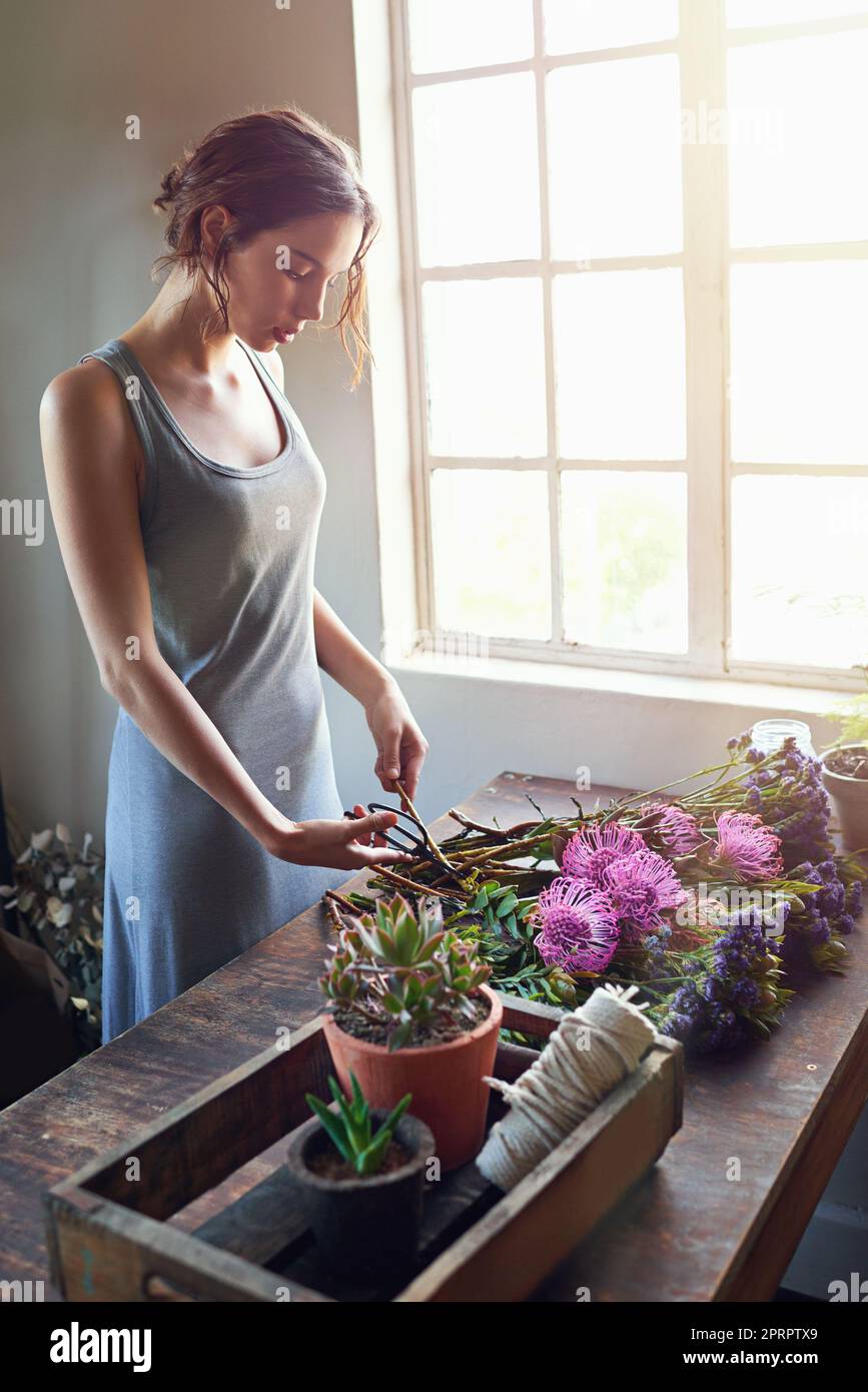 Rêvez, créez, inspirez. Un jeune fleuriste coupant des fleurs pour composer un comptoir de bouquet. Banque D'Images