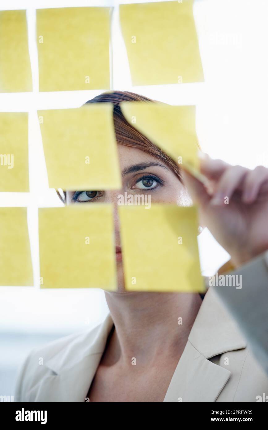 Visualiser ses pensées. Une femme d'affaires organisant des notes collantes sur un mur de verre. Banque D'Images