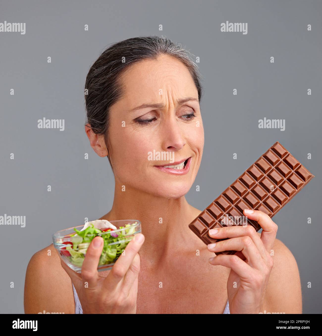 C'est une décision vraiment difficile. Photo studio d'une belle femme mûre qui décide entre une salade et du chocolat Banque D'Images