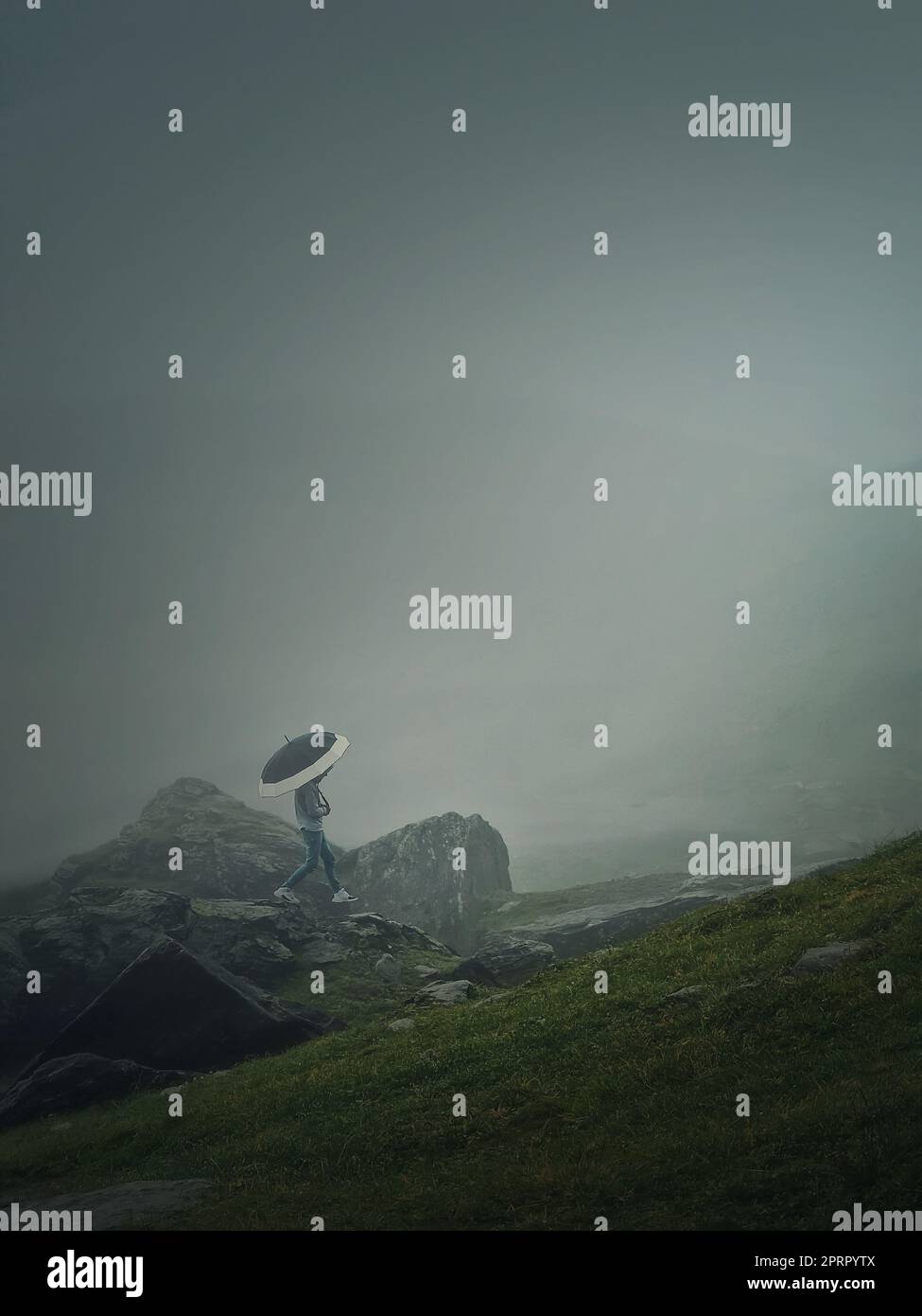 Homme avec un parapluie grimpant une colline de montagne par temps sombre avec une brume dense. Scène de randonnée Moody avec une marche de Wanderer sur les falaises de la vallée de foggy Banque D'Images