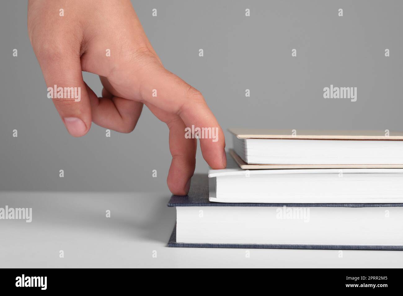 Femme imitant monter sur des livres avec ses doigts contre fond gris, gros plan Banque D'Images