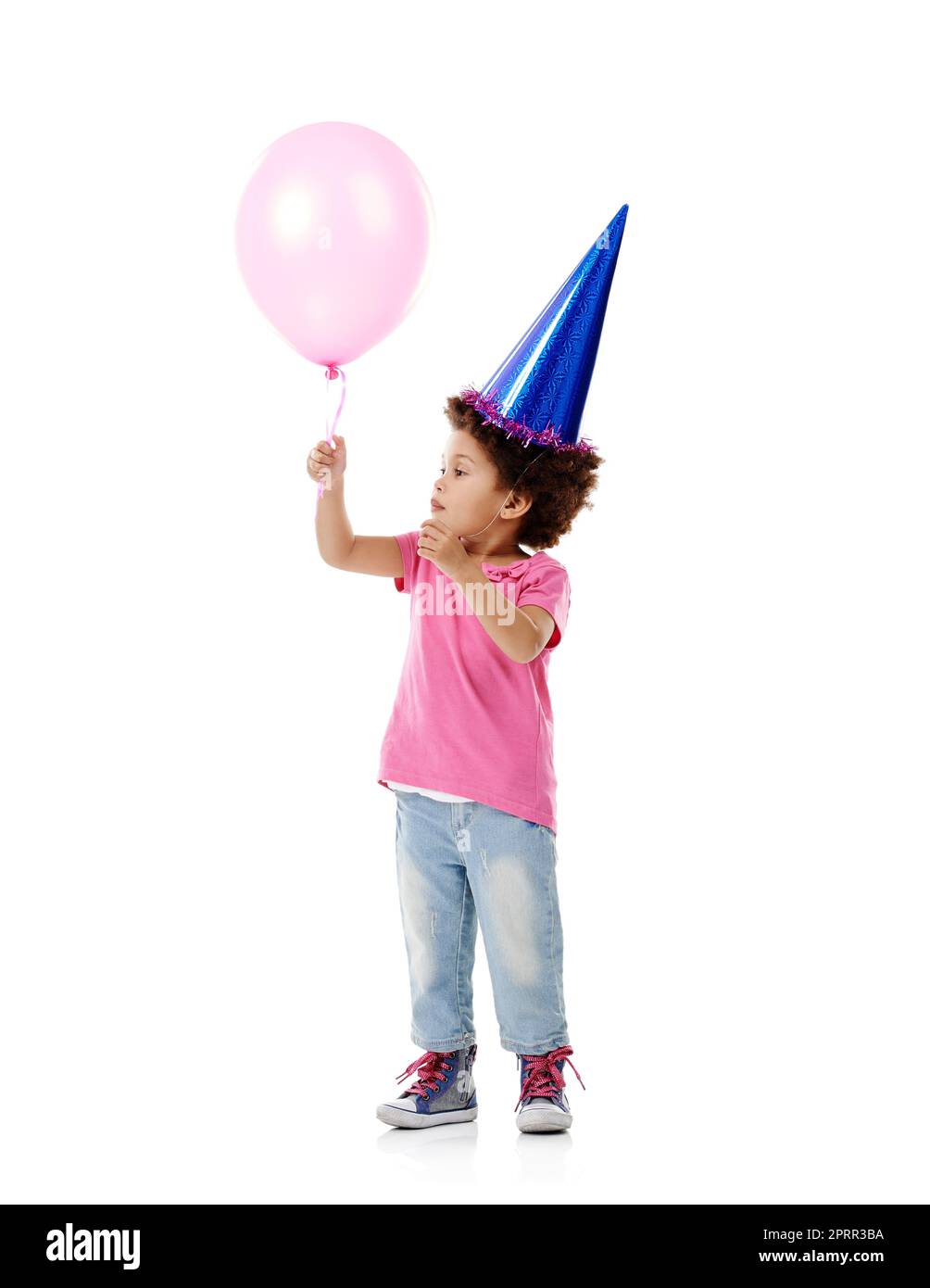 Je me demande si je pouvais flotter loin sur cette chose... Studio photo d'une petite fille mignonne portant un chapeau de fête et tenant un ballon sur un fond blanc. Banque D'Images