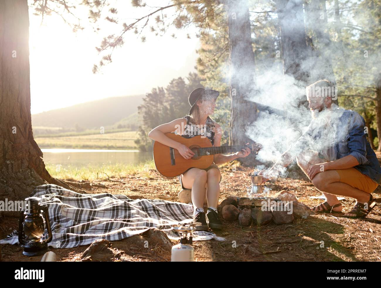 Feux de camp. une jeune femme jouant de la guitare pour son petit ami à leur campement Banque D'Images