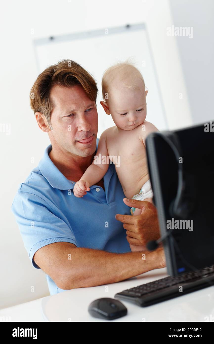 Multitâche comme un patron. Un père tenant un petit enfant tout en essayant de travailler. Banque D'Images