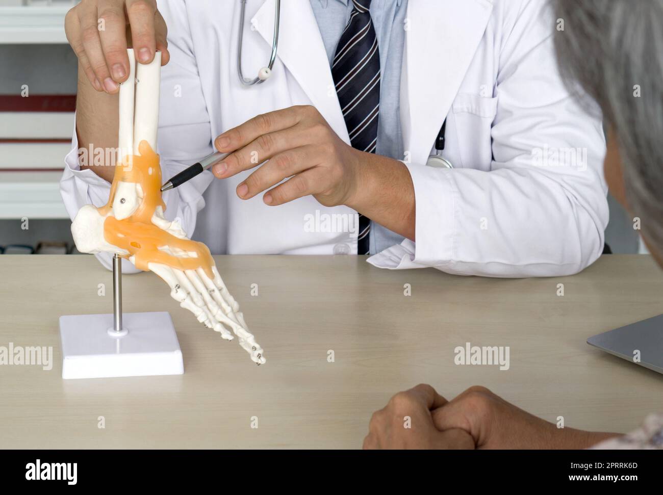 Chirurgien orthopédique en robe blanche et stéthoscope pointant sur le squelette humain pied cheville os modèle anatomique d'articulation, présenter au patient âgé au sujet du traitement de la cheville avec la chirurgie. Banque D'Images