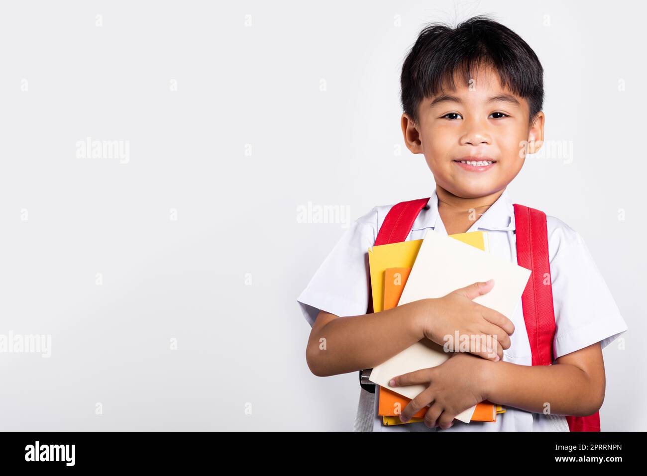 Asiatique adorable tout-petit souriant Happy Wear étudiant thaïlandais uniforme rouge pantalon tenir ou serrer livre Banque D'Images