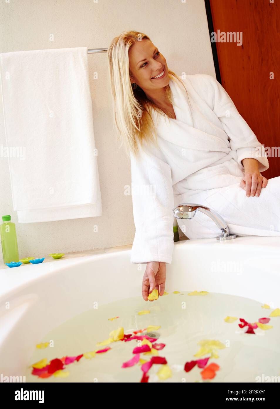 Faites de votre maison un spa. Une belle jeune femme assise sur le bord d'un bain luxueux rempli de pétales Banque D'Images