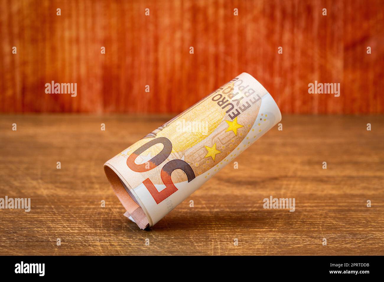 Rouleau de cinquante billets en euros tombant sur fond de bois Banque D'Images