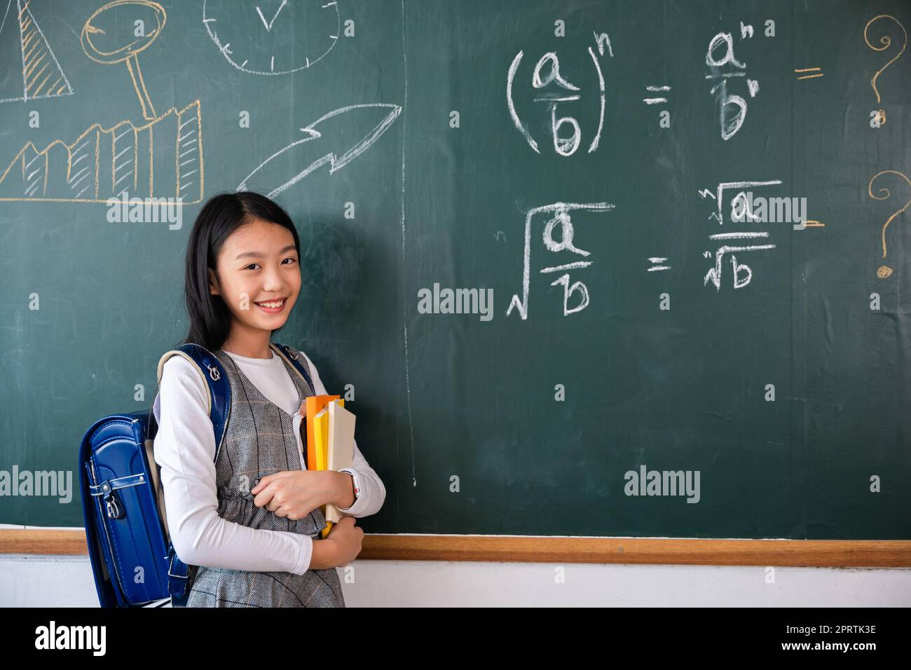 Heureuse belle fille d'école asiatique debout tenant des livres debout devant le tableau noir de la salle de classe Banque D'Images